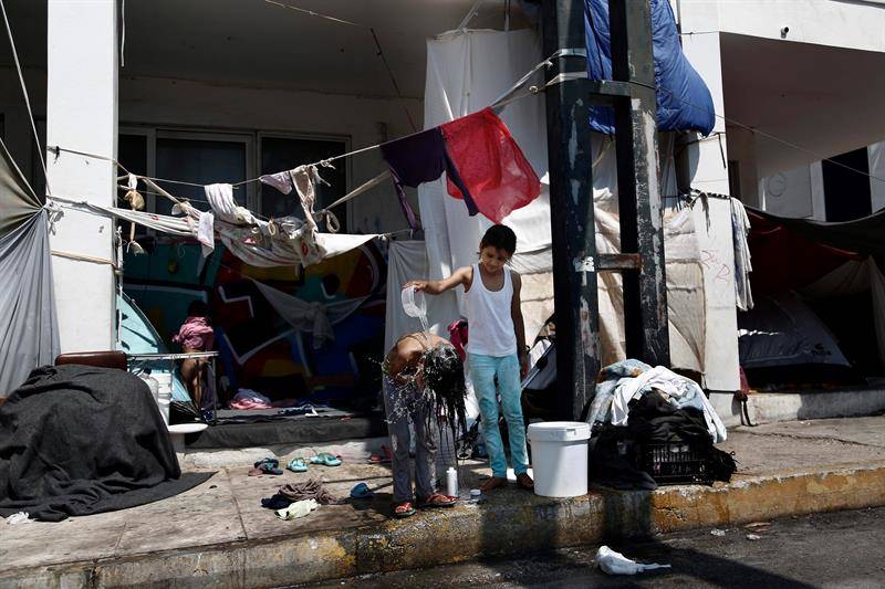 23/08/2016. Una niña afgana ayuda a su hermana a lavarse delantede su tienda en los alrededores del antiguo aeropuerto internacional de Atenas (Grecia) donde refugiados y migrantes se alojan, hoy, 23 de agosto de 2016. El alto comisionado de las Naciones Unidas para los refugiados, Filippo Grandi, inicia hoy una visita de tres días de duración a la capital helena para conocer las necesidades humanitarias de los refugiados y migrantes que se encuentran en el país (Foto: EFE)